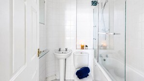Et badeværelse med en brusekabine i glas, en hvid vask og et toilet.