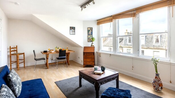 En stue med sofa, sofabord, spisebord, stole og et stort vindue med udsigt til bygninger.