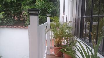 Een overdekt terras met plantenpotten, een witte balustrade en uitzicht op groen.