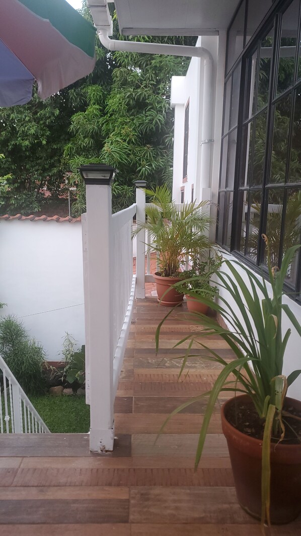 Een overdekt terras met plantenpotten, een witte balustrade en uitzicht op groen.