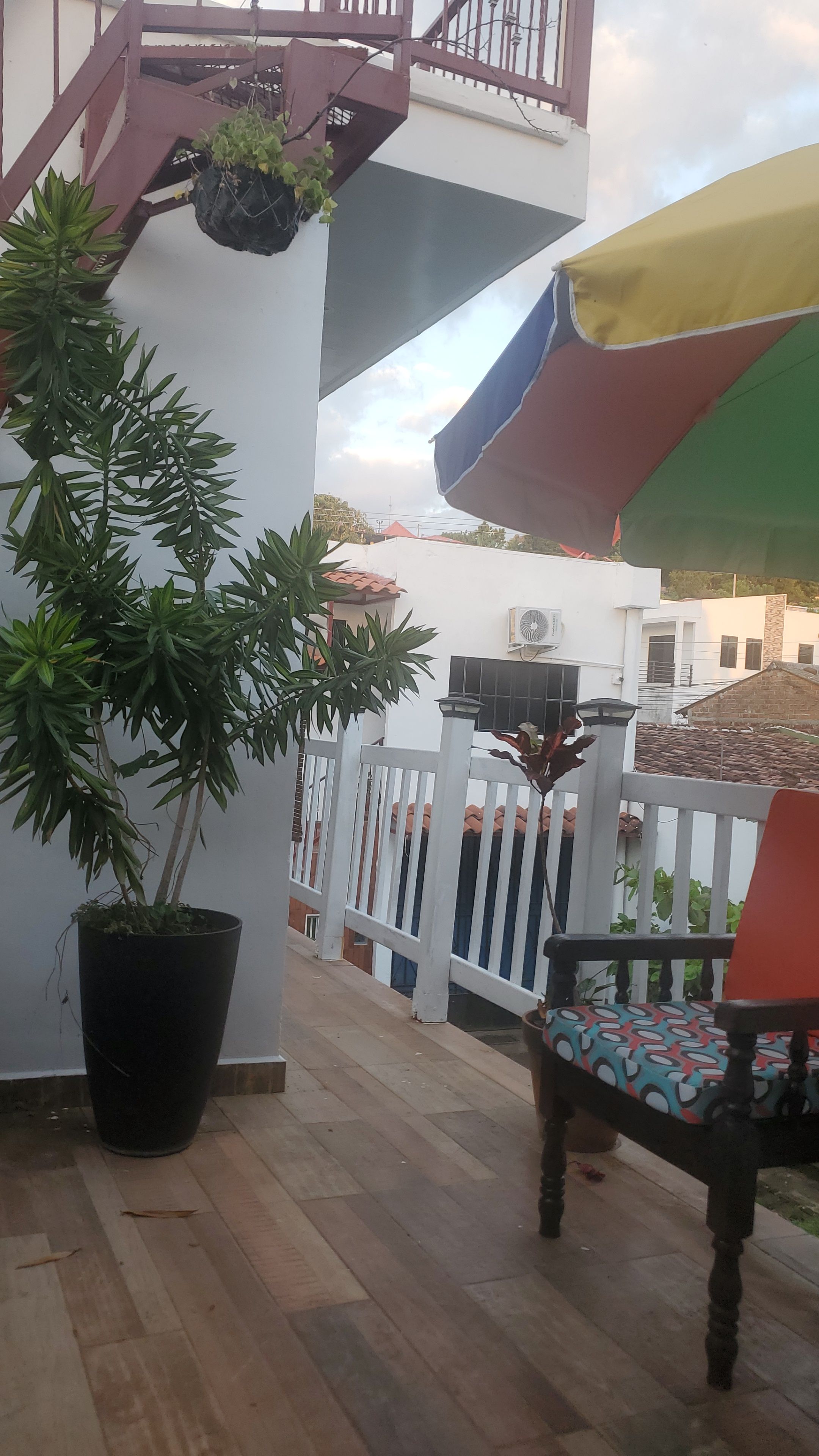 Een houten terras met een bloempot, een wit hek en een kleurrijke parasol.