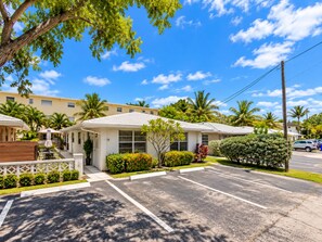 A hotel with a parking lot, a covered outdoor seating area, and a view of palm trees and other greenery. - NEW! Modern Coastal 5BR, Sunset Villa Near Beach (Pompano Beach)