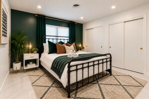 A modern bedroom with a bed, bedside tables, a nightstand, a potted plant, and a window with curtains. - NEW! Modern Coastal 5BR, Sunset Villa Near Beach (Pompano Beach)