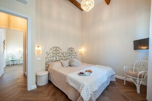 Ein Schlafzimmer mit Bett, Nachttischlampen, einem Fernseher, einem Sessel und einem kleinen Tisch mit Speisen.