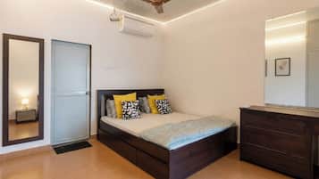 A bedroom with a bed, bedside table, wardrobe, ceiling fan, and an air conditioning unit.