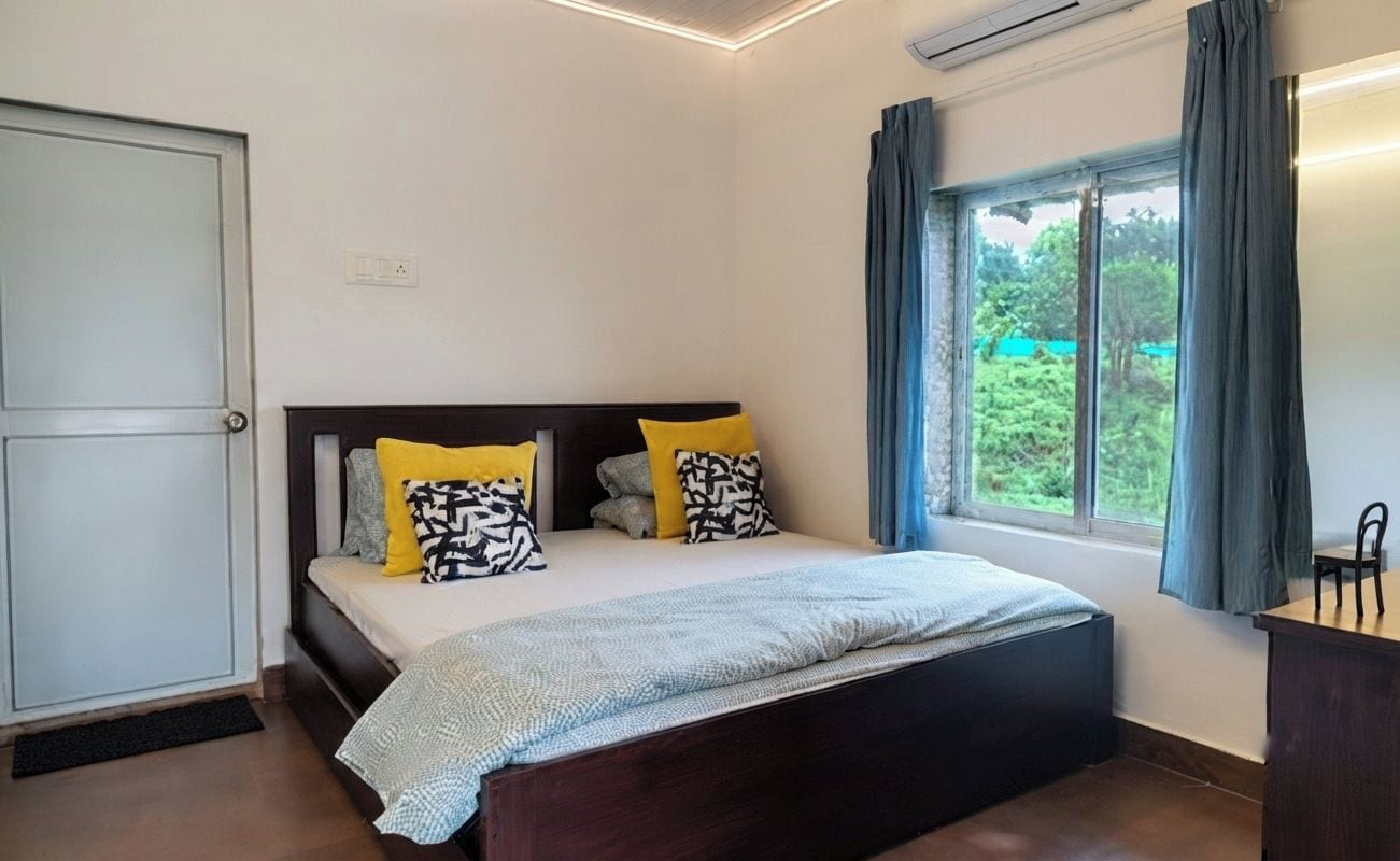 A bedroom with a bed, a bedside table, a window with curtains, and a door.