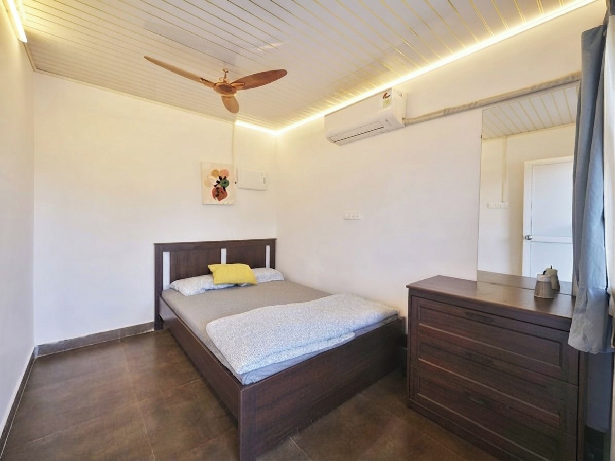 Una camera da letto con un letto, una ventola a soffitto, un condizionatore d'aria, un comò e uno specchio.