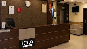 Un mostrador de recepción de hotel con un reloj, un cartel de 'No Fumar' y un cartel con los horarios de registro.