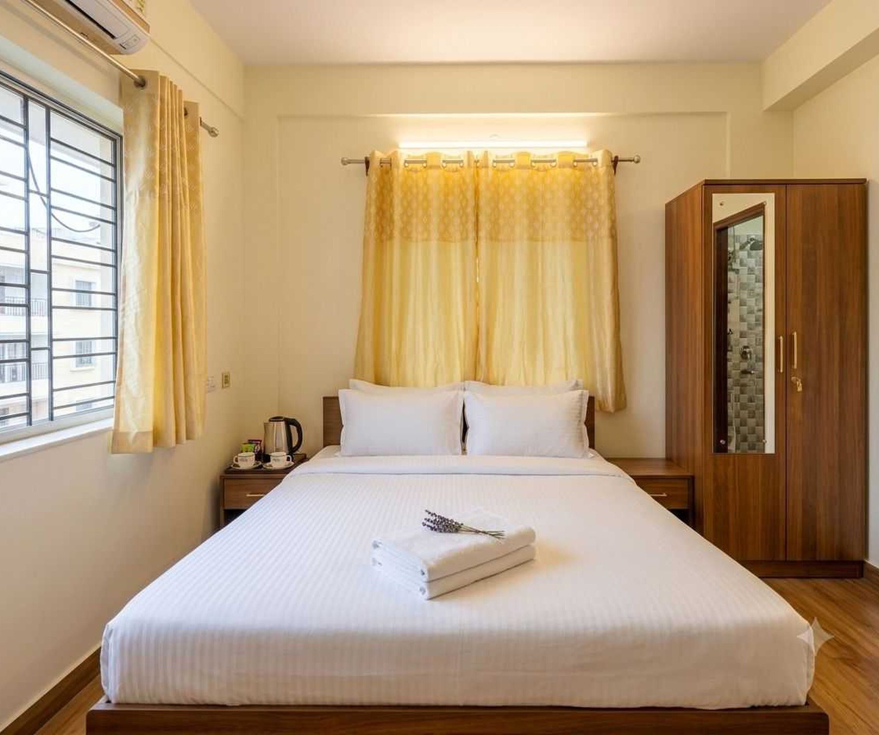 A hotel room with a bed, a nightstand, a wardrobe, and a window with curtains.