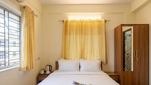 Una habitación de hotel con cama, mesita de noche, armario y ventana con cortinas.
