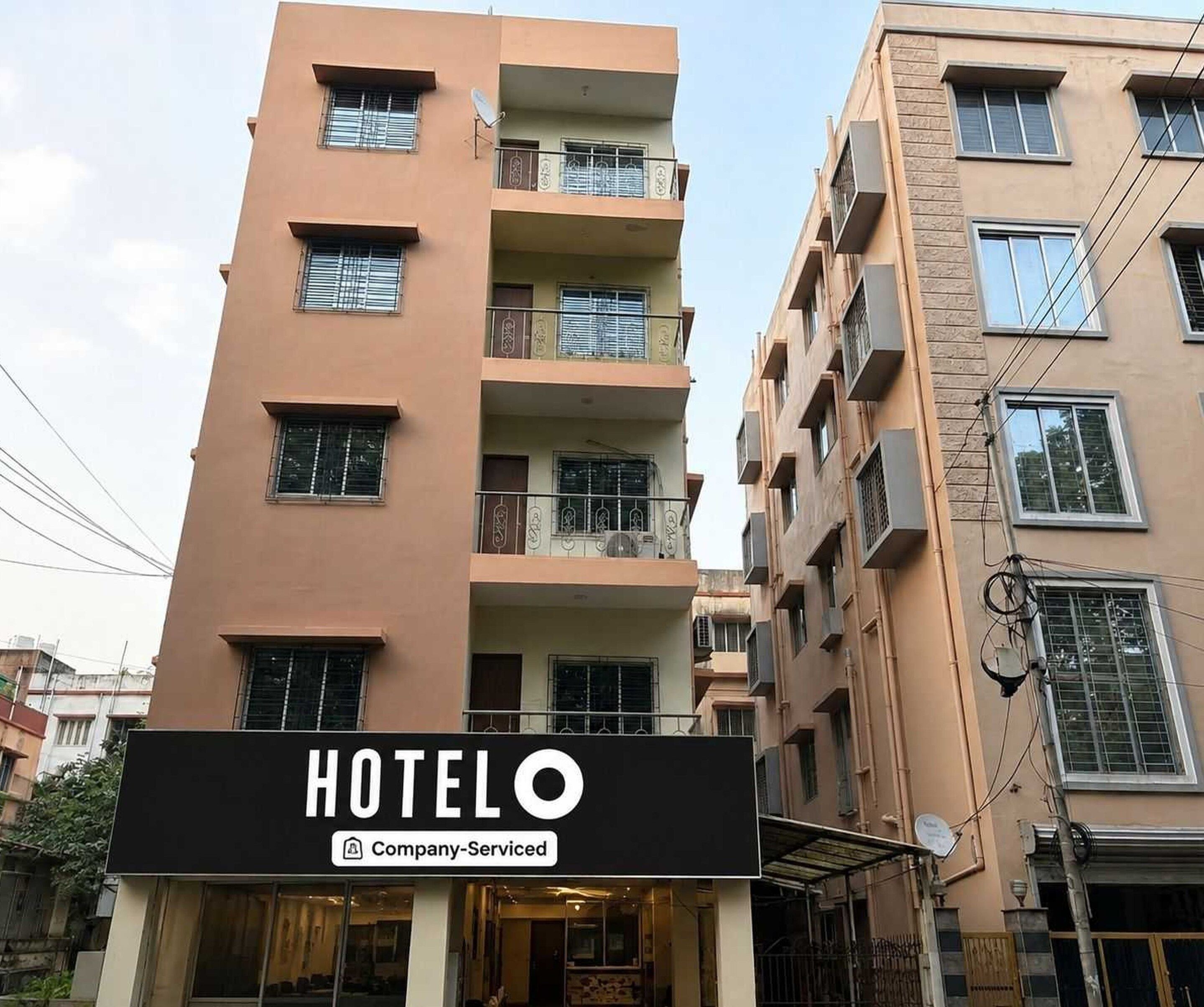 A hotel building with multiple floors, balconies, and a sign indicating it is a company-serviced hotel.