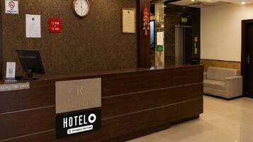 A hotel reception desk with a clock, a no-smoking sign, and a sign indicating check-out times.