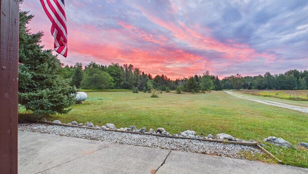 A residential property with a view of a field and trees, a concrete driveway, and an American flag. - UP Getaway - Pictured Rocks and Hiawatha National Forest awaits you! (Munising)