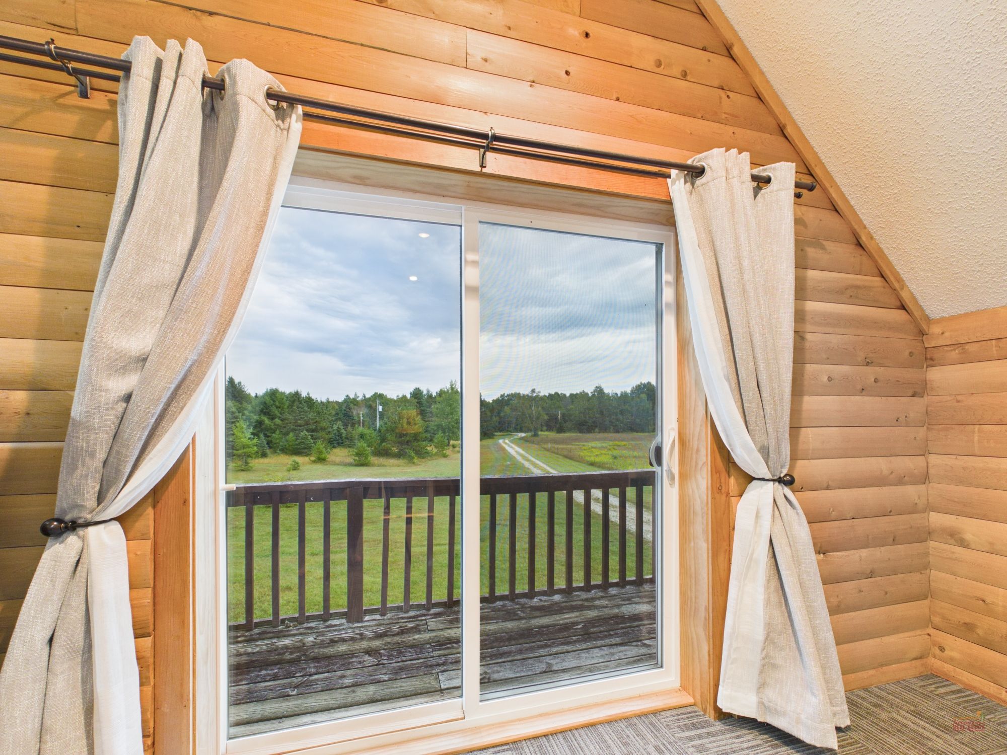 A room with a large sliding glass door leading to a balcony with a view of a grassy field and trees.