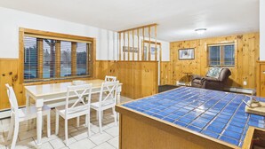 A room with a dining table, chairs, a wooden partition, and a blue-tiled counter. - UP Getaway - Pictured Rocks and Hiawatha National Forest awaits you! (Munising)