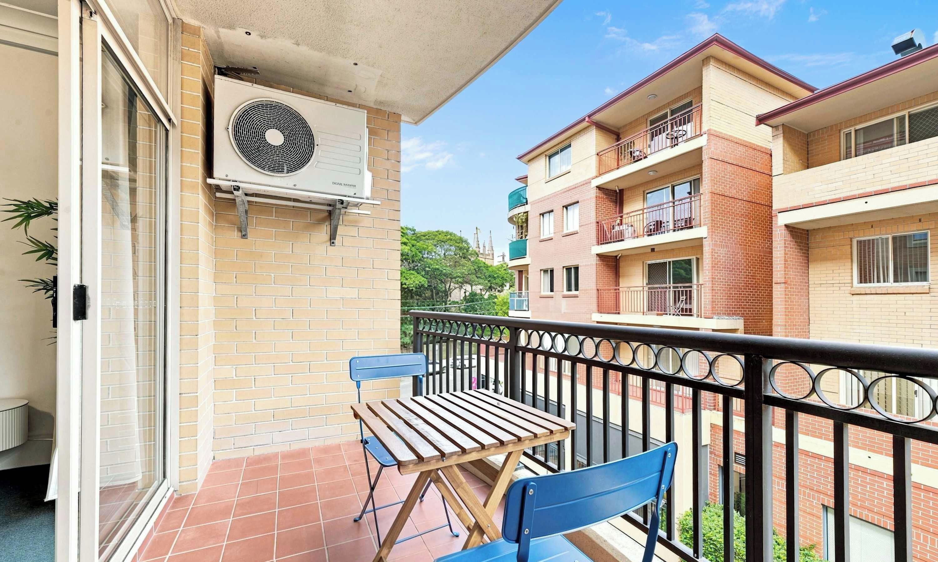 A balcony with a table and chairs, a window, and an air conditioning unit.