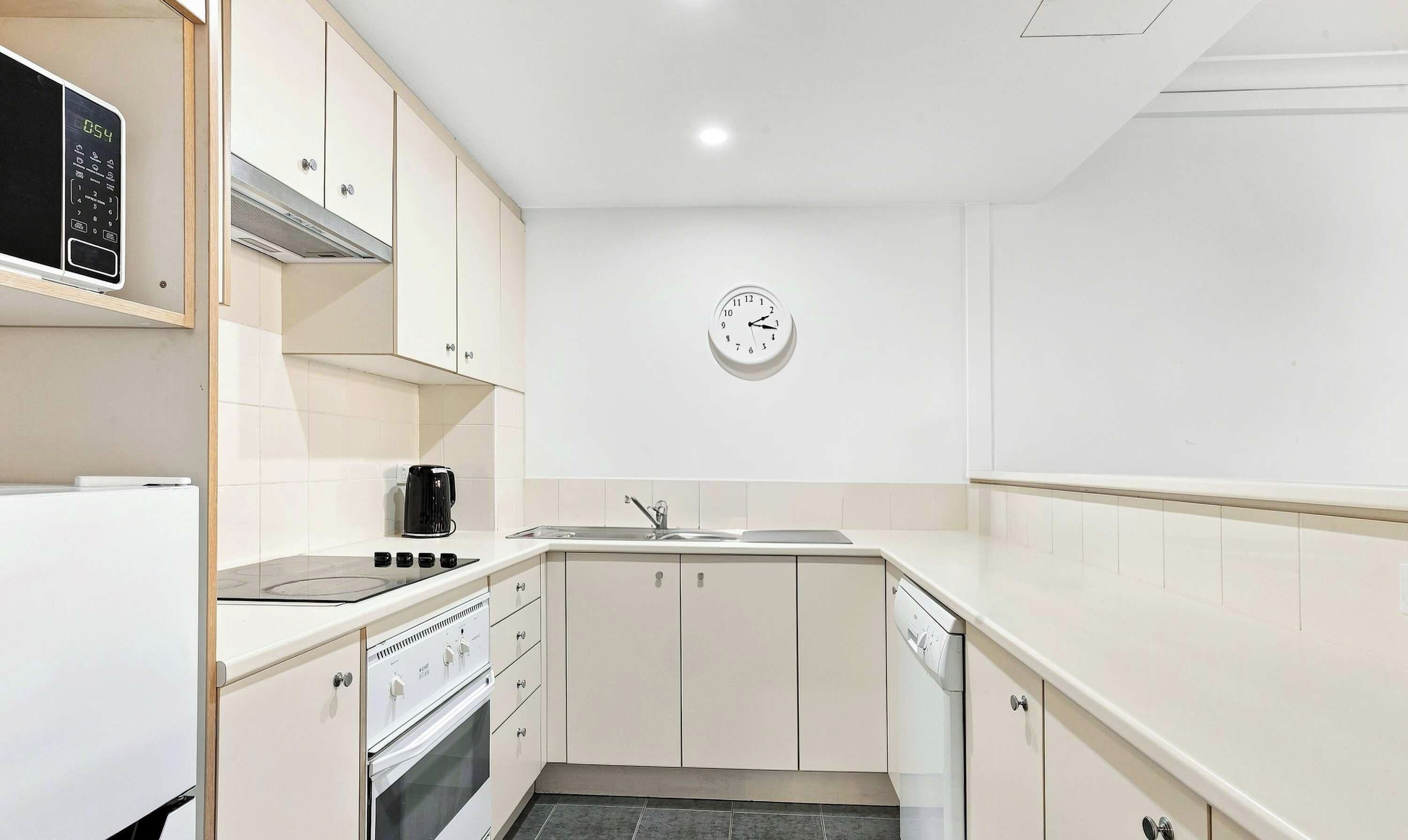 A compact kitchen with white cabinets, a built-in oven, a microwave, a coffee maker, and a sink.