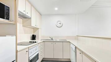 A compact kitchen with white cabinets, a built-in oven, a microwave, a coffee maker, and a sink.