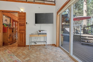 A room with a wooden floor, a flat-screen TV mounted on the wall, and a wooden cabinet with a plant. - House of Stone and Light: Your Four-Season Sanctuary in Angel Fire, New Mexico (Angel Fire)