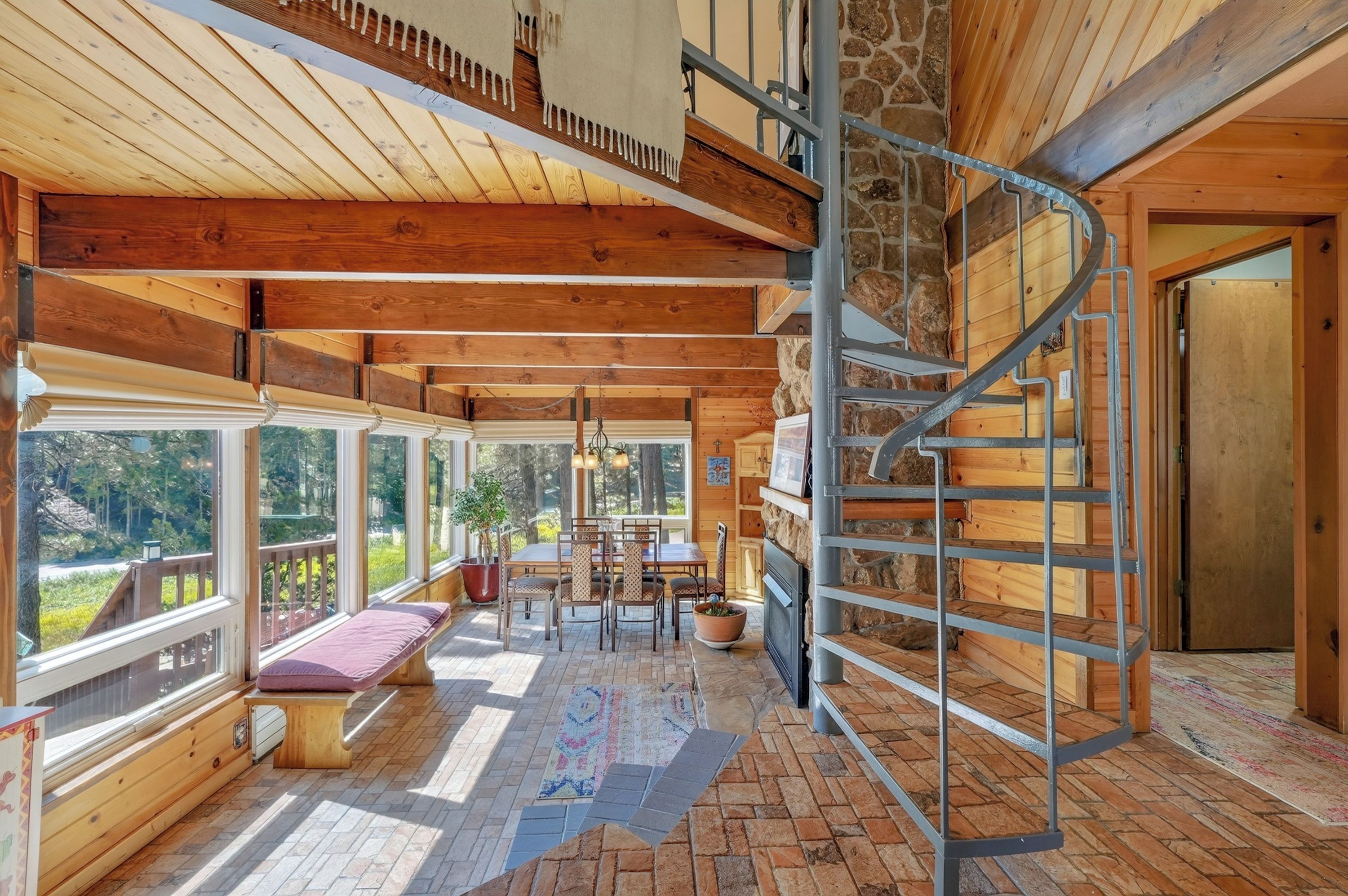 A wooden cabin interior with a spiral staircase, large windows, and a fireplace.