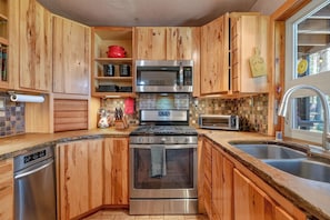 A compact kitchen with wooden cabinets, stainless steel appliances, and a tiled backsplash. - House of Stone and Light: Your Four-Season Sanctuary in Angel Fire, New Mexico (Angel Fire)