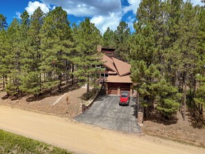 A two-story house with a garage, surrounded by pine trees, and a paved driveway leading to the entrance. - House of Stone and Light: Your Four-Season Sanctuary in Angel Fire, New Mexico (Angel Fire)