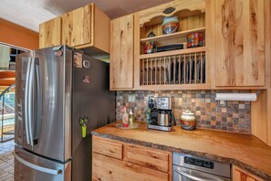 A kitchen with wooden cabinets, a stainless steel refrigerator, a coffee maker, and a dishwasher. - House of Stone and Light: Your Four-Season Sanctuary in Angel Fire, New Mexico (Angel Fire)