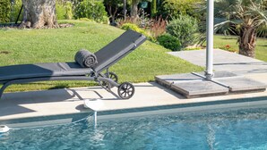 A poolside area with a lounge chair and an umbrella, a tree, and a view of a hilly landscape. - Melinda - Super Cannes (Vallauris)