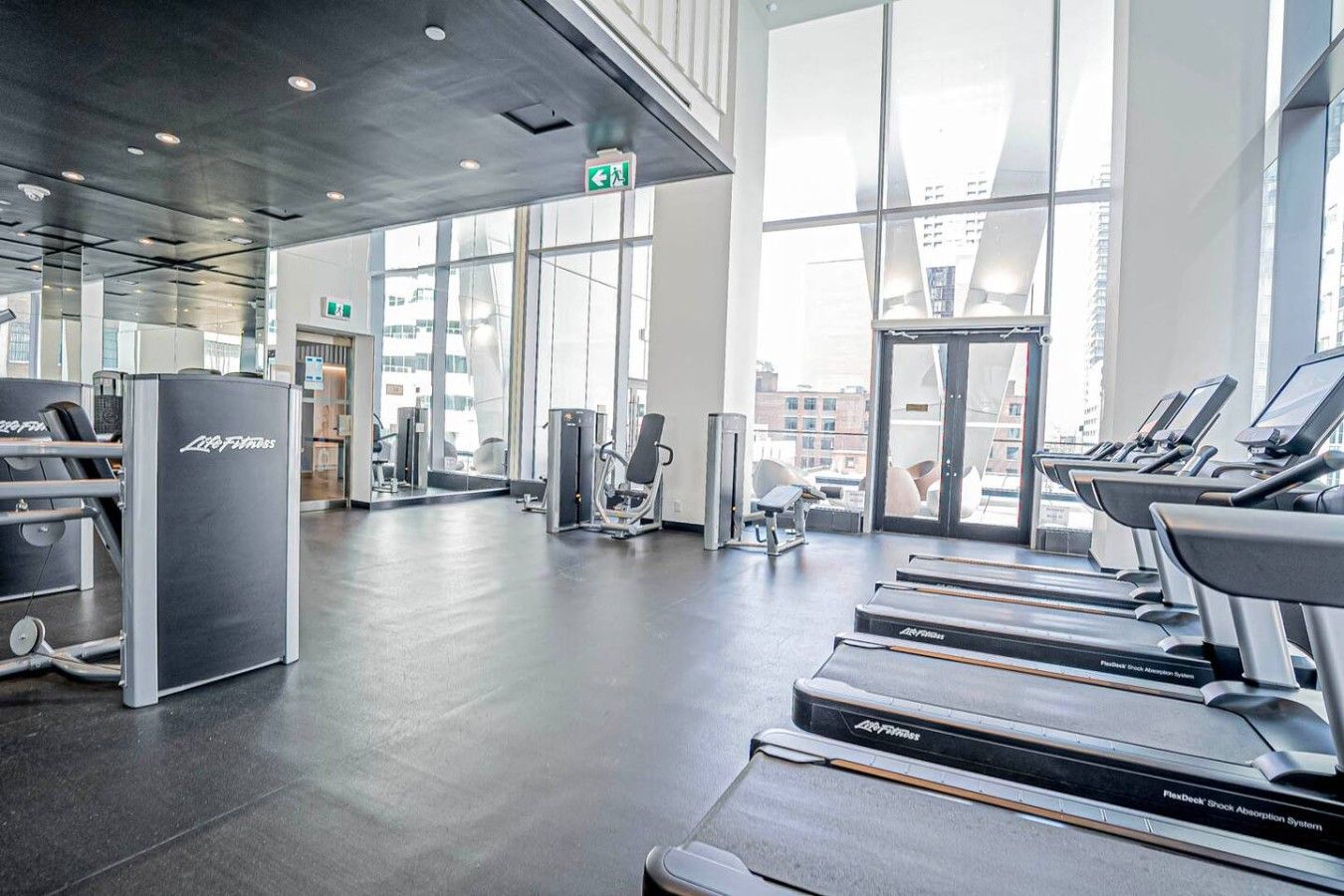 Une salle de sport équipée de tapis de course, d’appareils de musculation et d’une grande fenêtre offrant une vue sur la ville.
