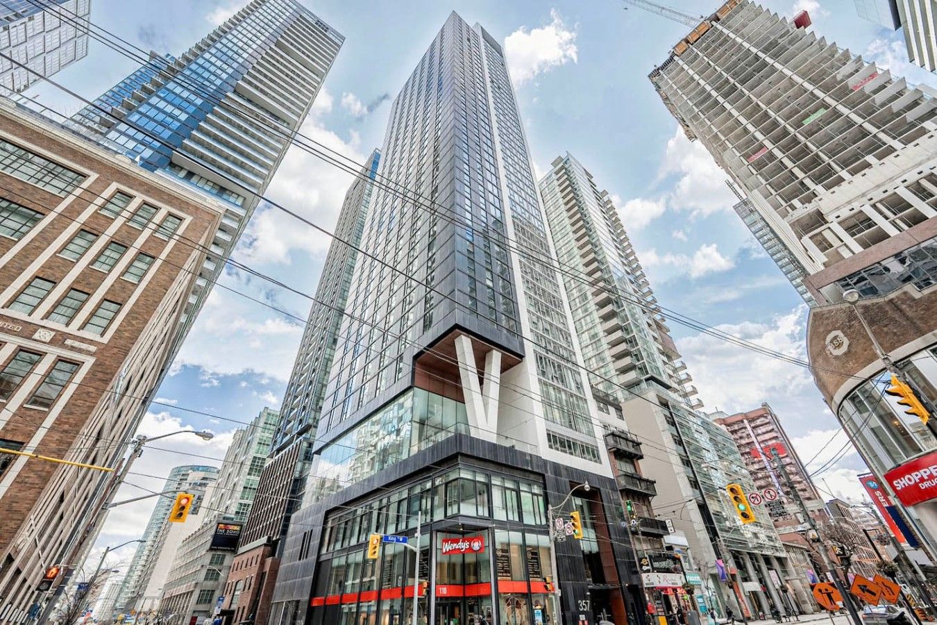 A high-rise building with a modern glass facade, surrounded by other tall buildings and a street with visible traffic lights and storefronts.