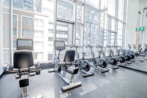 A gym with cardio machines and weight stations, large windows, and a visible exit sign. - Luxury King West Suite | 2BR + 2BA | Gym (Toronto)