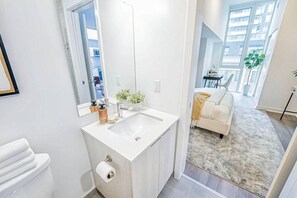 A modern bathroom with a large mirror, white sink, and a toilet. - Luxury King West Suite | 2BR + 2BA | Gym (Toronto)