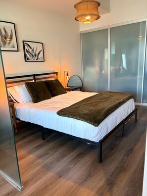 Une chambre à coucher comprenant un lit, une tête de lit, une table de chevet, une lampe et un tableau accroché au mur.