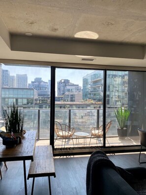 Un balcon spacieux offrant une vue sur la ville, aménagé avec une table, des chaises et des plantes en pot.