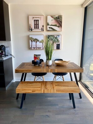 A dining area with a wooden table and benches, a coffee machine, and framed artwork on the wall. - Stylish King West Condo with Balcony (Toronto)