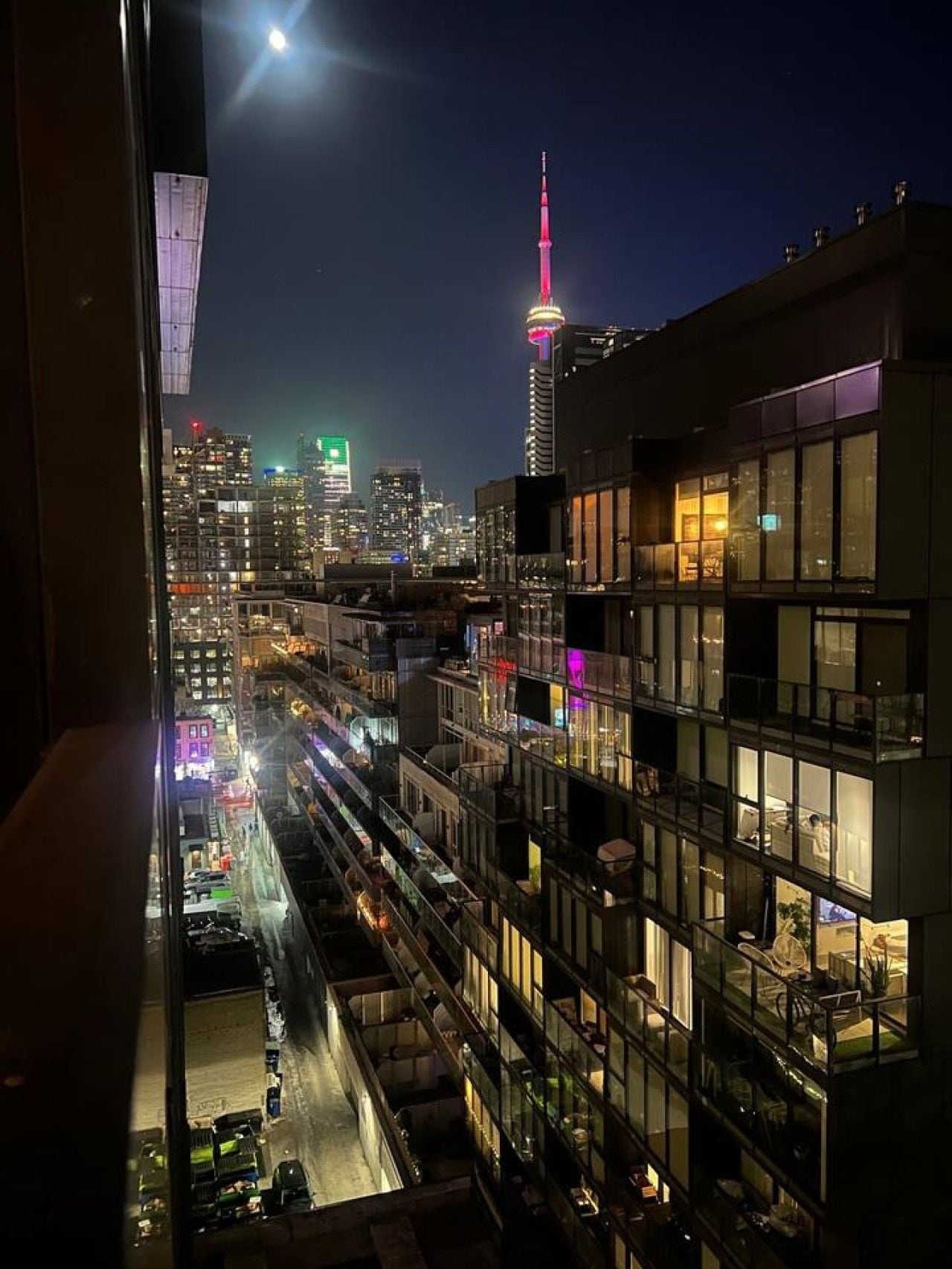 Een stadsgezicht bij nacht met een opvallende toren en een gebouw met meerdere verdiepingen en balkons.