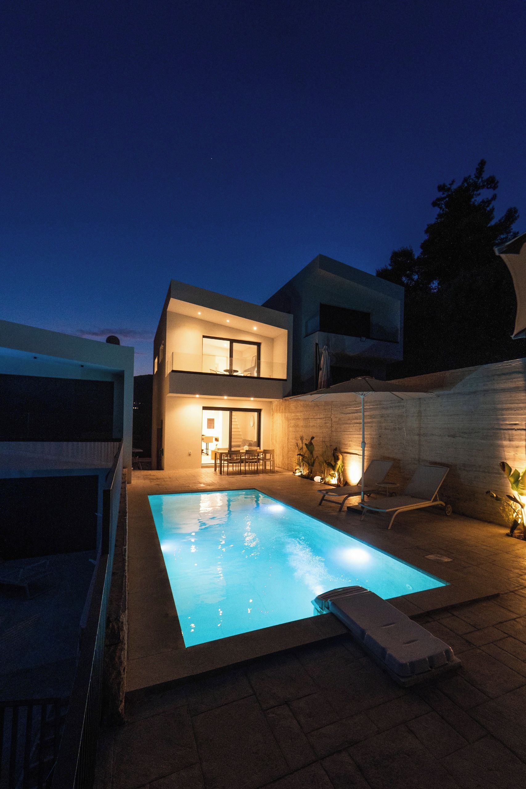A modern two-story house with a swimming pool, outdoor seating, and a staircase leading to the upper level.