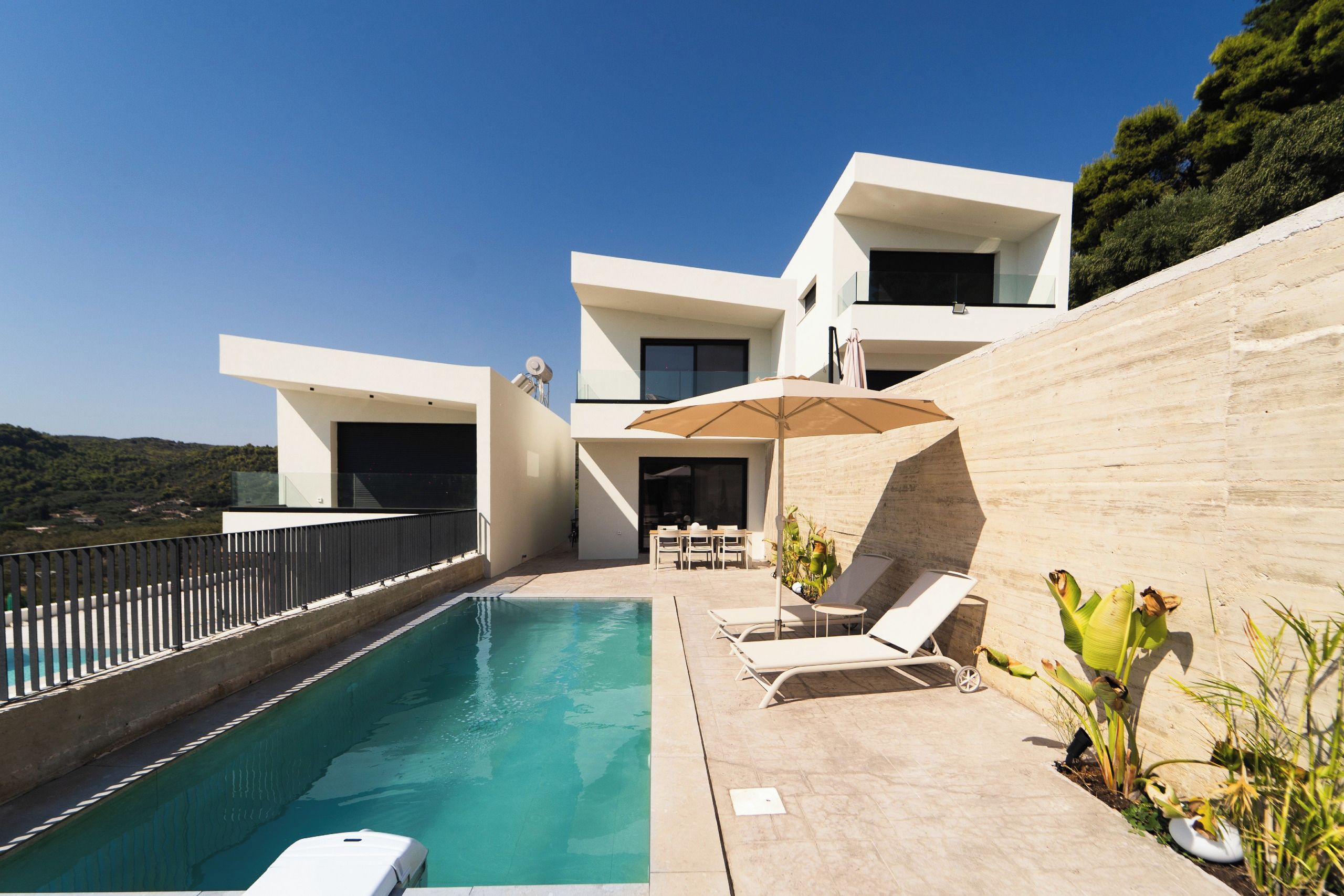 Eine moderne Villa mit Swimmingpool, Sitzgelegenheit im Freien und Blick auf die umliegende Landschaft.