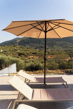 A terrace with lounge chairs and a large umbrella, overlooking a hilly landscape with olive groves and scattered buildings. - A Cube Villa - Two Bedroom Villa, Sleeps 5 (Keri)