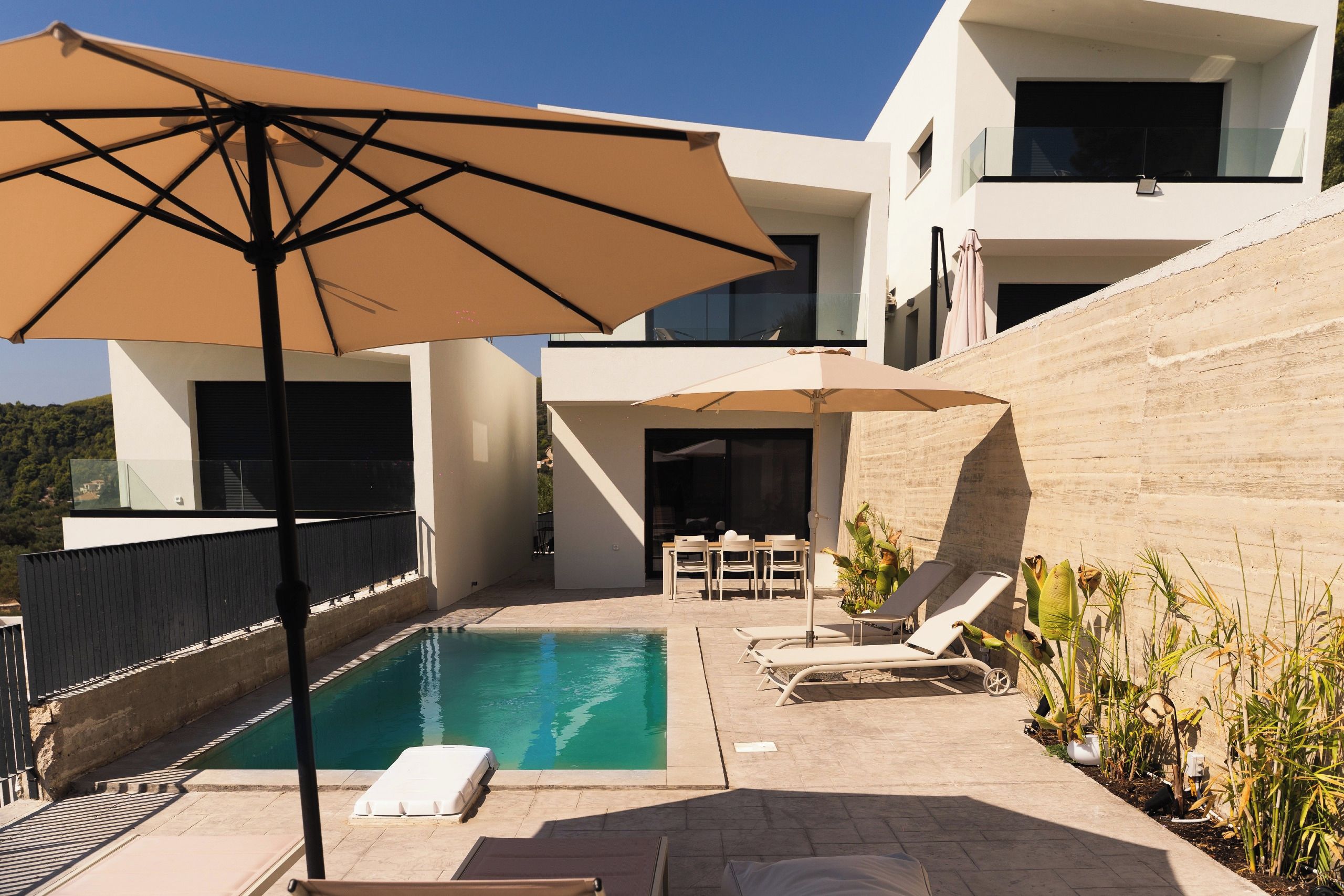Un espace piscine extérieur moderne, doté de chaises longues et d’un parasol.