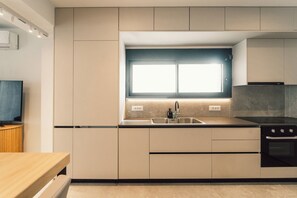 A modern kitchen with a built-in oven, a sink with a window above it, and a wooden dining table. - A Cube Villa - Two Bedroom Villa, Sleeps 5 (Keri)