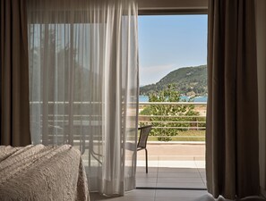 A room with a bed, a chair, and a balcony with a view of the sea and hills. - Avesta Private Villas Kallisto (Lefkada)