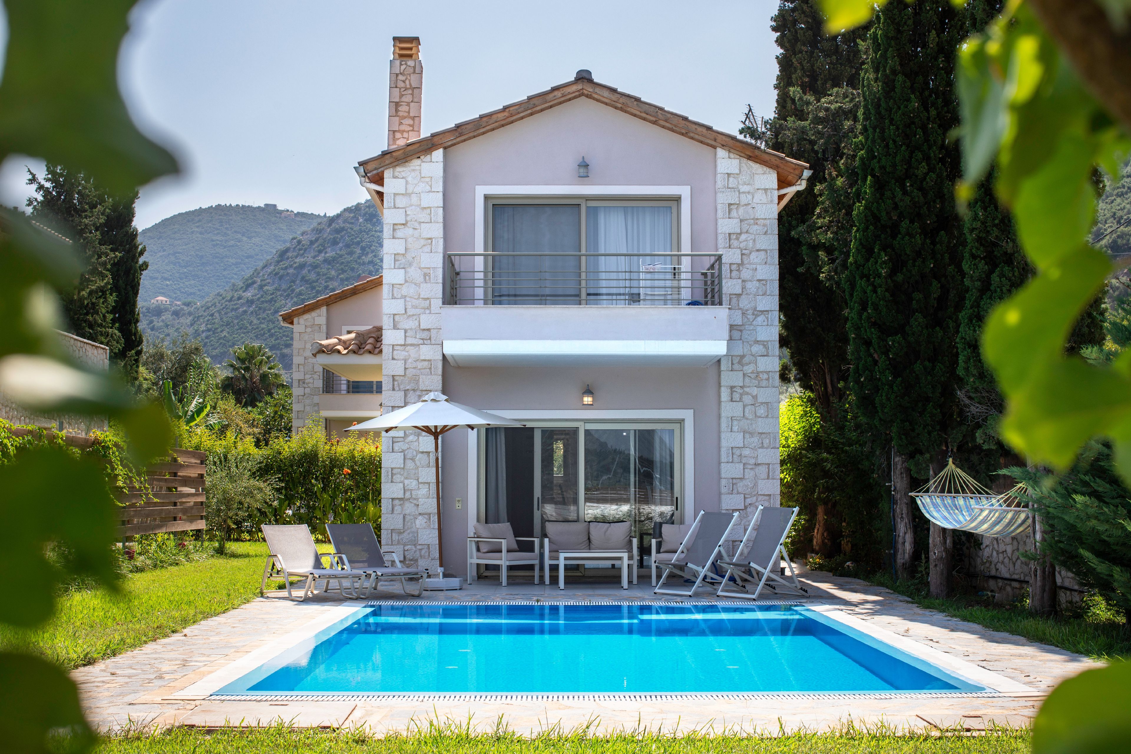 Una casa de dos pisos con piscina, mobiliario exterior y vistas a las montañas.