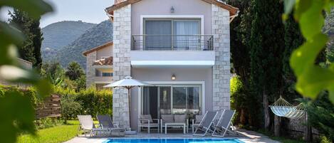 A two-story house with a swimming pool, outdoor seating, and a view of the mountains.