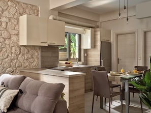 A modern kitchen with a stone accent wall, a central island, and a dining area with chairs and a table. - Avesta Private Villas Kallisto (Lefkada)