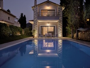 Ein zweigeschossiges Haus mit einer Naturstein-Fassade, einem Balkon mit Sitzgelegenheiten und einem Schwimmbecken im Vordergrund.