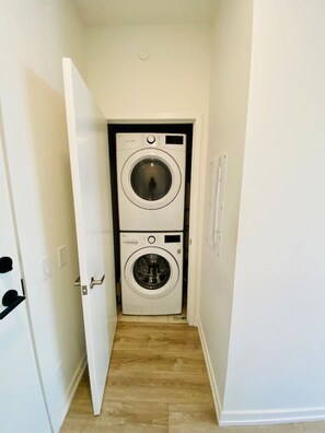 Une buanderie équipée de deux machines à laver à chargement frontal superposées, d’un plancher en bois et d’une porte blanche.