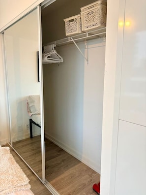 Un dressing accessible sans porte, doté d’une porte coulissante en verre, d’un plancher en bois et d’un mur blanc.