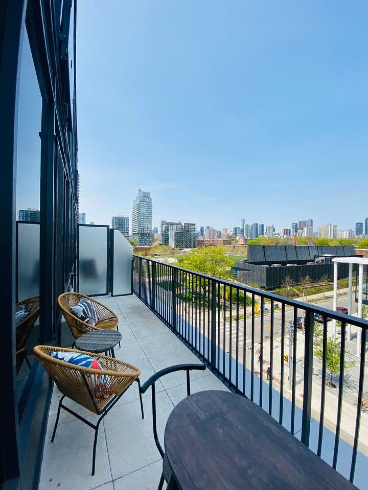 A balcony with a view of a city skyline, wicker chairs, a table, and a metal railing.