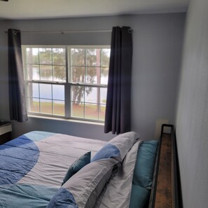 A bedroom with a bed, a window with curtains, and a view of trees outside. - Guest house on the lake. Trailer parking available (Deltona)